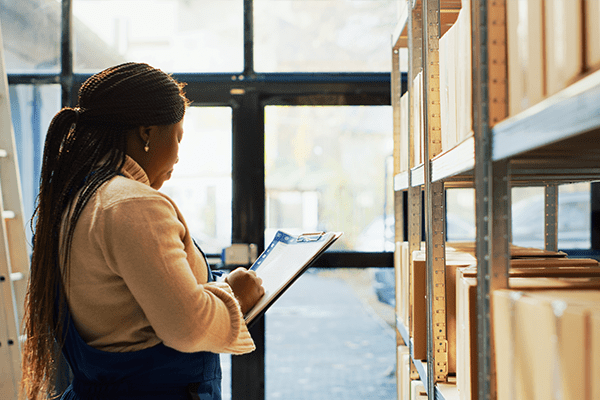 Woman of color in warehouse looking at clipboard